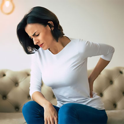 Stock image of an woman in jeans and tshirt holding her back in sitting position and feeling kidney pain